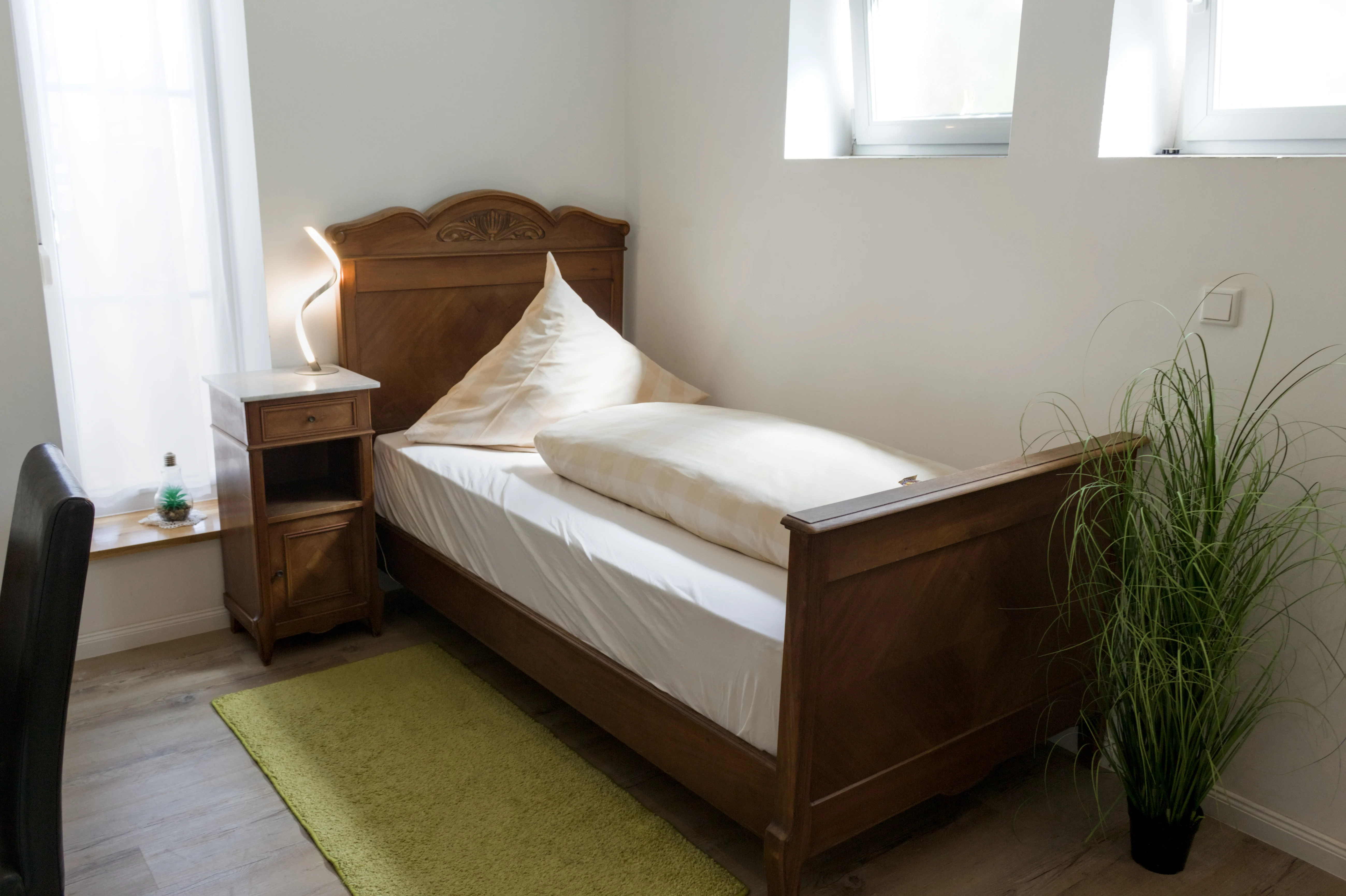 Einzelbett aus Holz mit Zimmerpflanze am Fenster