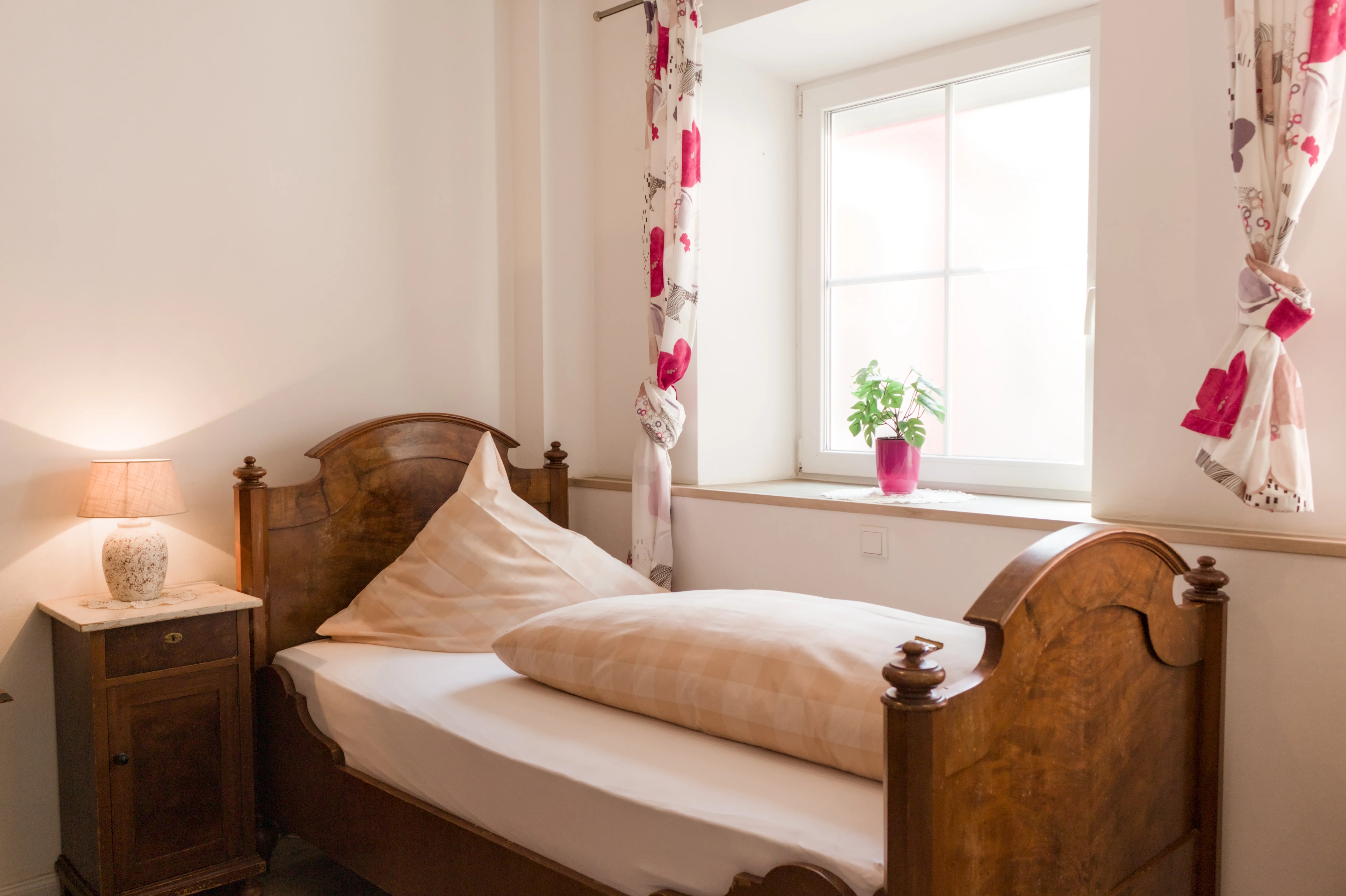 Einzelbett aus Holz am Fenster mit floralen Vorhängen
